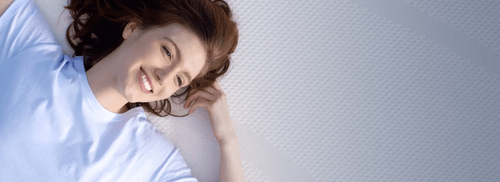 A close up view of a smiling woman laying on the Tempur-Cloud mattress